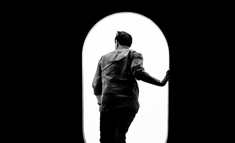 Photographie noir et blanc d'un homme qui rentre par une porte blanche aux bords arrondis